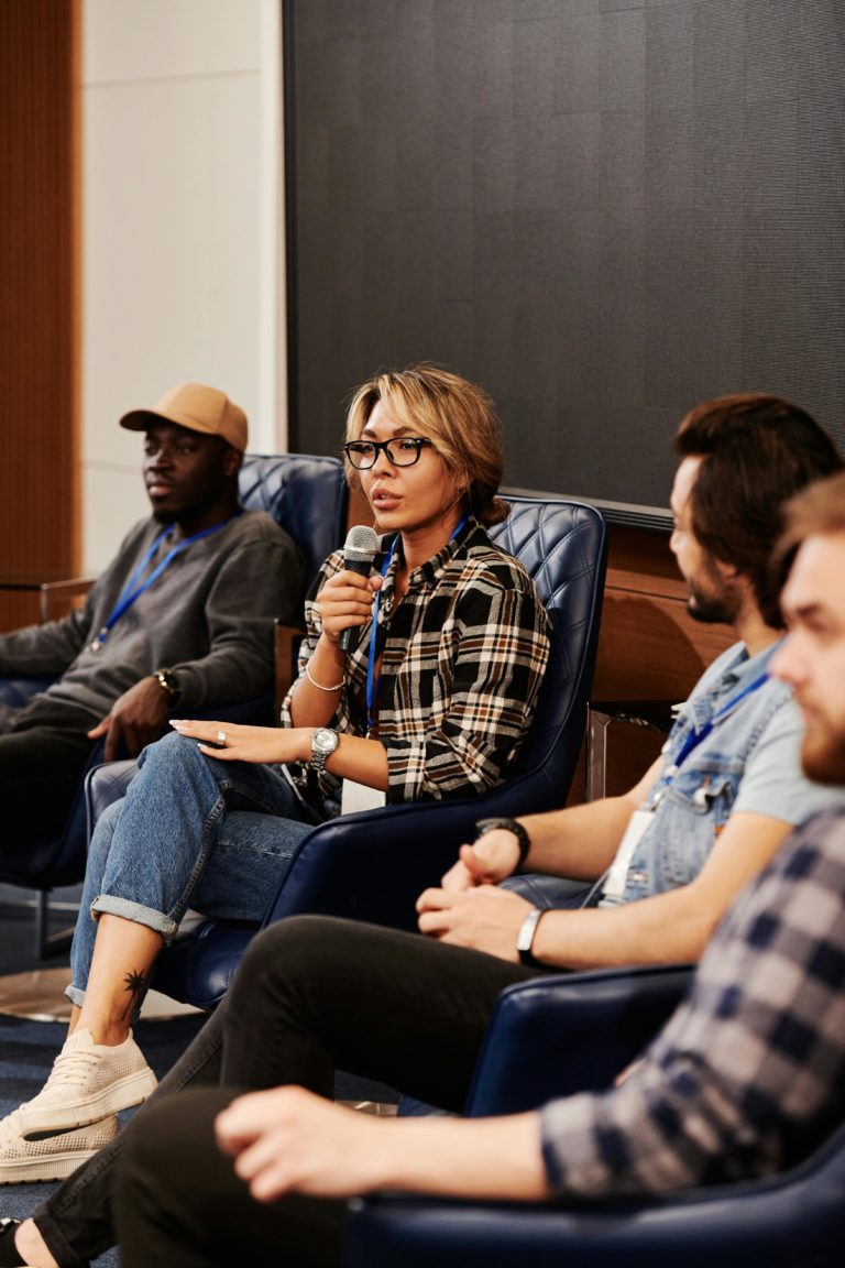 Quatre professionnels assis sur scène : une femme au centre tient un micro tandis que trois confrères l’écoutent attentivement dans une salle de conférence.
